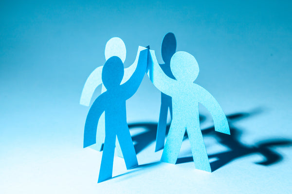 Blaue Papierfiguren von Menschen geben sich ein High-Five, symbolisch für Teamwork und Zusammenarbeit.
