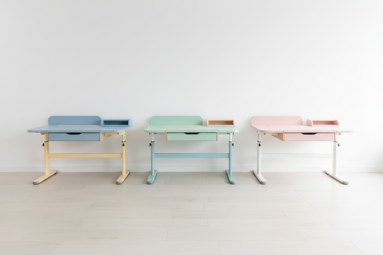 Drei höhenverstellbare Kinderschreibtische in Pastellfarben (blau, mint, rosa) vor weisser Wand auf hellem Boden.