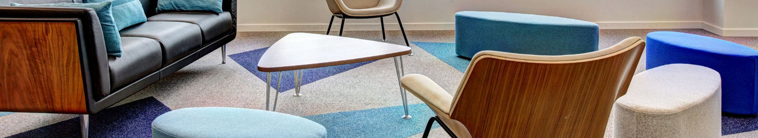Lounge-Bereich mit Sofa, Sessel, kleinem Tisch und bunten Polsterhockern auf gemustertem Teppich.