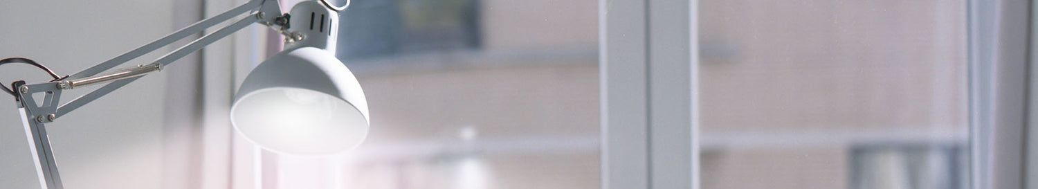 Weisse Schreibtischlampe mit Gelenkarm und rundem Lampenschirm vor unscharfem Hintergrund.