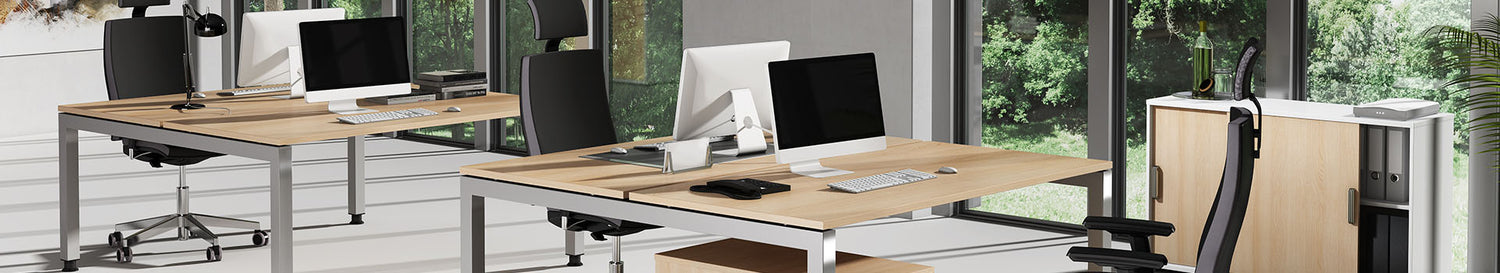 Modernes Büro mit zwei Schreibtischen in Holzoptik, Monitoren, ergonomischen Bürostühlen und Sideboard vor grossen Fenstern mit Blick ins Grüne.