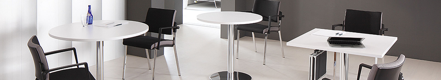 Modernes Besprechungszimmer mit runden und eckigen weissen Tischen, schwarzen Stühlen und hellen Bodenfliesen.