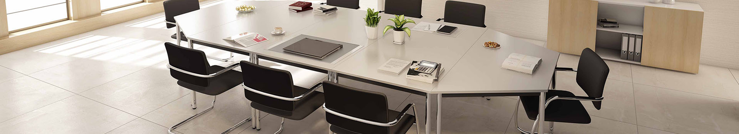 Grosses Besprechungszimmer mit modularem Konferenztisch, schwarzen Stühlen, Pflanzen und Unterlagen auf hellem Boden.
