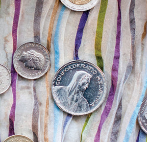 Alte, silberne Münzen liegen verteilt auf einem bunt gestreiften Untergrund
