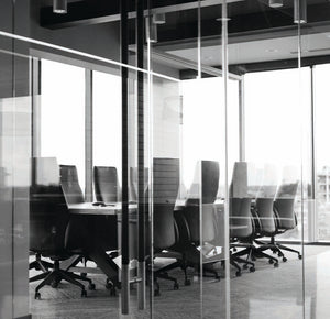 Blick in ein seriös und hochwertig wirkendes Büro hinter Glas mit schwarzen Bürostühlen um einen Sitzungstisch.